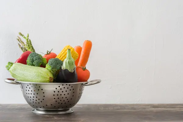 Vegetables in a colander on wood — Stock Photo, Image
