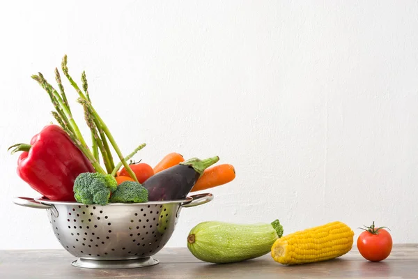 Vegetables in a colander on wood — Stock Photo, Image