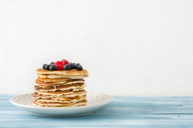 Yaban mersini ve ahududu üzerinde mavi tahta arka plan ile Pancakes 