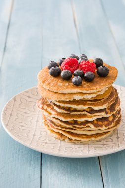 Yaban mersini ve ahududu üzerinde mavi tahta arka plan ile Pancakes 
