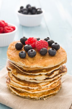Yaban mersini ve ahududu üzerinde mavi tahta arka plan ile Pancakes 