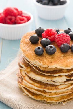Yaban mersini ve ahududu üzerinde mavi tahta arka plan ile Pancakes 
