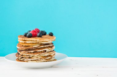 Yaban mersini ve ahududu üzerinde mavi arka plan ile Pancakes