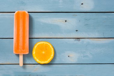 Mavi ahşap arka plan üzerinde turuncu çubuklu dondurmayı