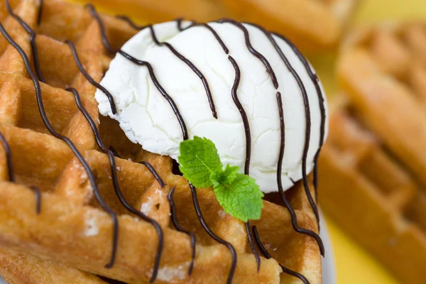 Gaufres à la sauce au chocolat, crème glacée et menthe sur bois rustique sur fond jaune — Photo