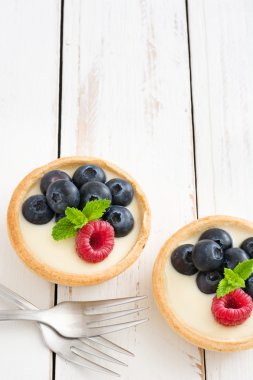 Ahududu ve beyaz tahta üzerinde yaban mersini ile lezzetli tartlets