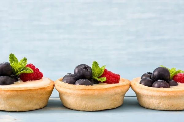 Deliciosas tartaletas con frambuesas y arándanos sobre fondo azul —  Fotos de Stock