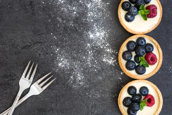 Deliciosas tartaletas con frambuesas y arándanos sobre fondo de pizarra —  Fotos de Stock