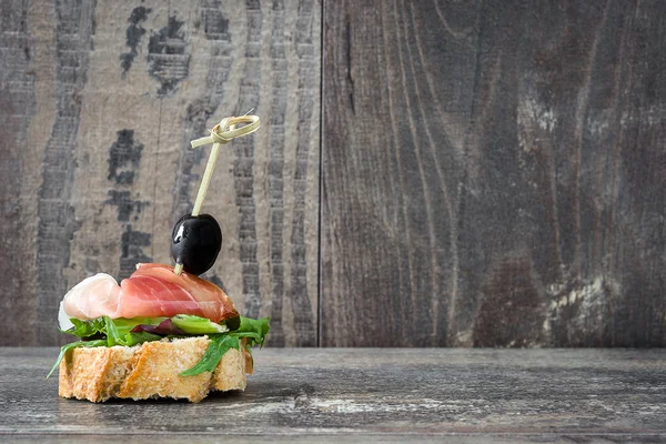 Испанский серрано ветчина шампур с оливками и салатом на деревенском деревянном фоне — стоковое фото