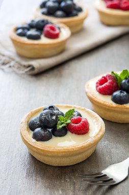 Ahududu ve rustik ahşap bir masa üzerinde yaban mersini ile lezzetli tartlets
