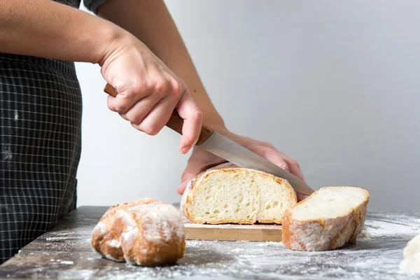 Mujer cortando pan en una mesa de madera rústica — Foto de Stock