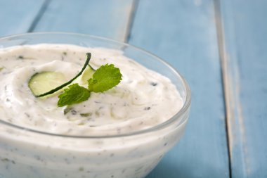 Mavi ahşap bir masa üzerinde bir kapta Tzatziki sos