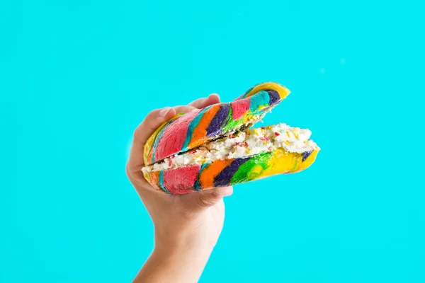 Panecillo colorido con queso y salpicaduras en la mano sobre fondo azul —  Fotos de Stock