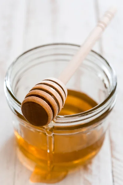 stock image Honey dipper with honey in a jar on white wooden table