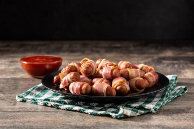 Battaniyeli domuz. Ahşap masada füme pastırmaya sarılmış sosisler.