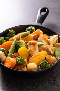 Tavuğu sebzeyle karıştır, siyah arka planda demir tavada.