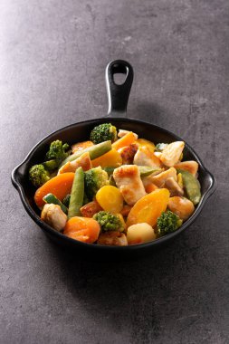 Tavuğu sebzeyle karıştır, siyah arka planda demir tavada.