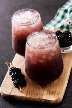 Siyah arka planda soğuk bardakta taze böğürtlen kokteyli.