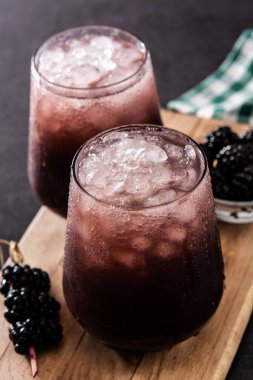 Siyah arka planda soğuk bardakta taze böğürtlen kokteyli.