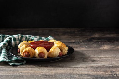 Battaniyeli domuzlar. Tahta masada ketçap soslu puf böreğe sarılı mini sosisler.