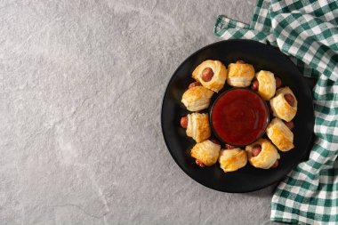 Battaniyeli domuzlar. Gri taşlı arka planda ketçap soslu puf böreğe sarılı mini sosisler.