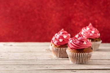 Sevgililer Günü için ahşap masa ve kırmızı arka planda şeker kalplerle süslenmiş kekler.