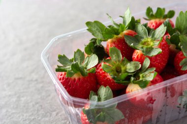 Gri taşlı arka planda plastik ambalajlı çilekler