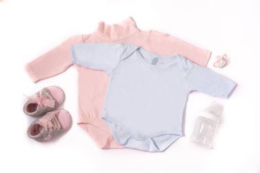 Bebek tulumları, ayakkabılar, beslenme şişesi ve emzik beyaz arka planda izole edilmiş.