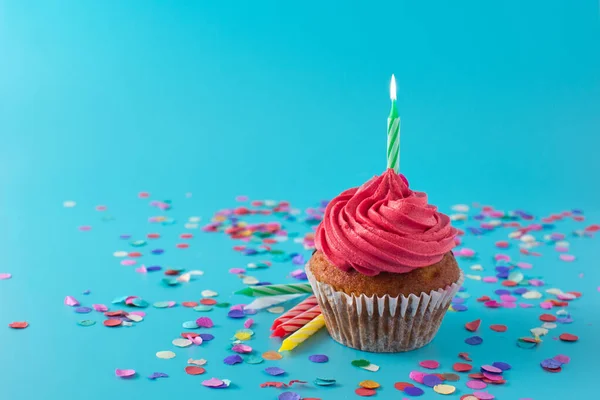 Pink birthday cupcake with green candle and confetti on blue background