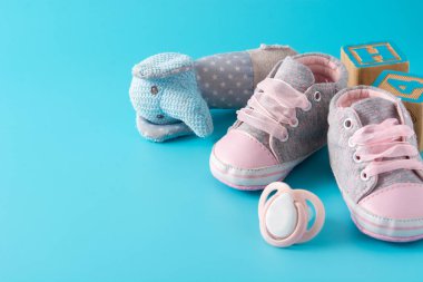 Bebek tulumları, ayakkabılar, beslenme şişesi, emzik ve oyuncak mavi arka planda. Boşluğu kopyala