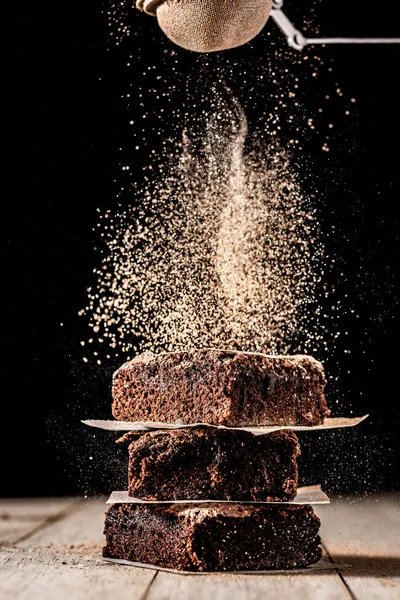Çikolata tozu brovnilerin üzerine yayılmış. Ahşap masa ve siyah arka plan.