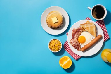 Geleneksel Amerikan kahvaltısı kızarmış yumurta, tost, domuz pastırması ve sosis ile mavi arka planda.