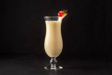 Siyah arka planda bir parça ananas ve kirazla süslenmiş Pina colada kokteyli.