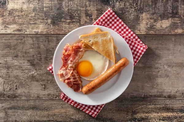 Traditional American breakfast with fried egg,toast,bacon and sausage on wooden table. Top view