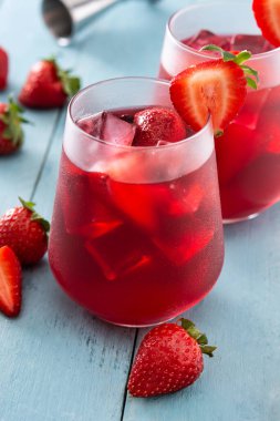 Mavi ahşap masada cam içinde çilek kokteyli.