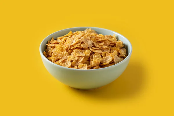 Corn flakes in a blue bowl on yellow background