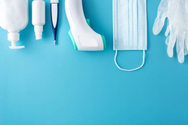 Tıbbi eldivenler, dezenfektan, termometre, el dezenfektanı ve mavi arka planda cerrahi maske. Boşluğu kopyala