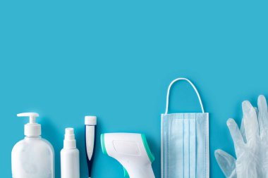 Tıbbi eldivenler, dezenfektan, termometre, el dezenfektanı ve mavi arka planda cerrahi maske. Boşluğu kopyala