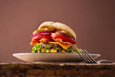 Ahşap masa ve kahverengi arka planda pastırmalı sığır etli burger.