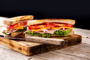 Domatesli sandviç, marul, jambon ve peynirli ahşap masa.