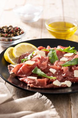 Siyah tabakta mermer et carpaccio ve kırsal ahşap masa.