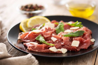 Siyah tabakta mermer et carpaccio ve kırsal ahşap masa.