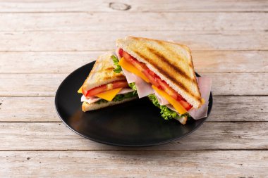 Domatesli sandviç, marul, jambon ve peynirli ahşap masa.