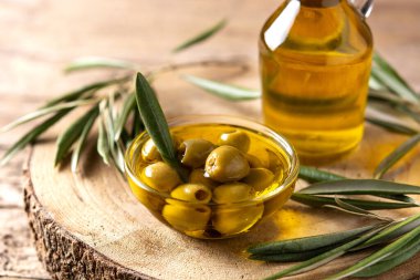 Bakire zeytin yağı şişesi ve ahşap masada yeşil zeytin.