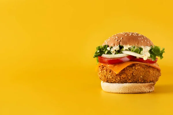 Crispy chicken burger with cheese on yellow background. Copy space
