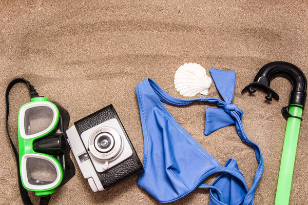 Old camera, bikini and shell on sand