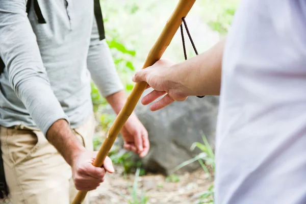 Uomo aiutare un altro dando un bastone per l'escursionismo — Foto Stock
