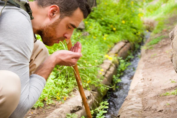 El hombre bebiendo agua del arroyo — Foto de Stock