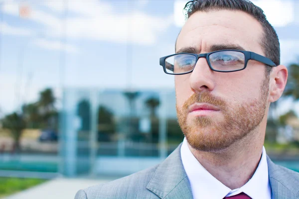 Businessman with glasses looking to the side with offices behind — Stock Photo, Image