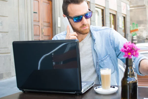 Bir dizüstü bilgisayar ve bir kahve bir teras üzerinde genç adam — Stok fotoğraf